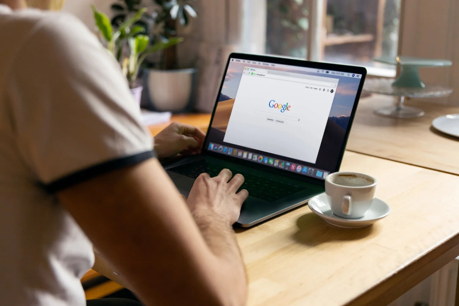 A person typing the keyboard of a laptop in a table with a cup