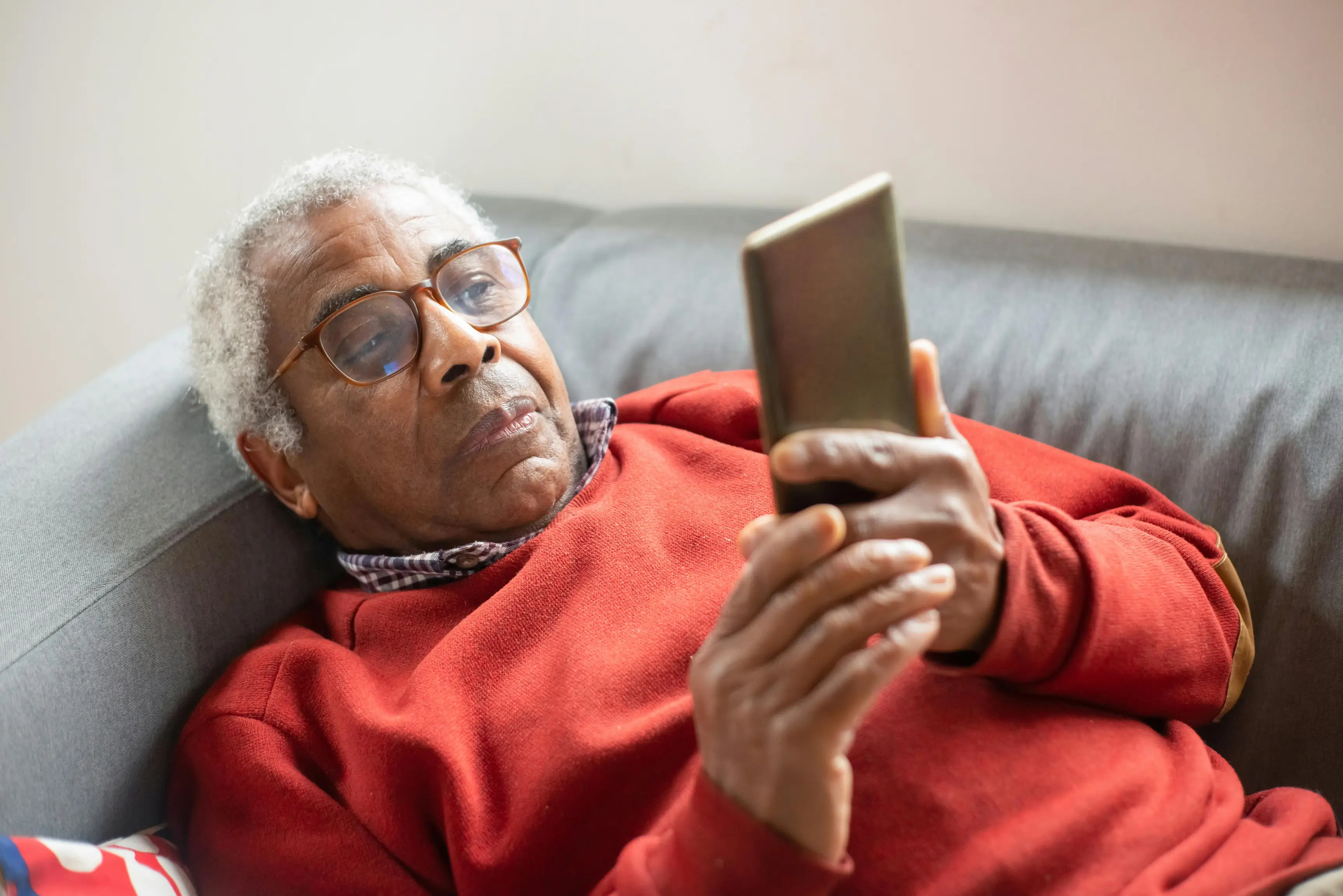 Elderly man lying on couch using smartphone