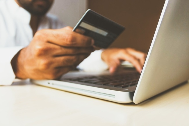 A hand holding a credit card and the other hand typing in a laptop