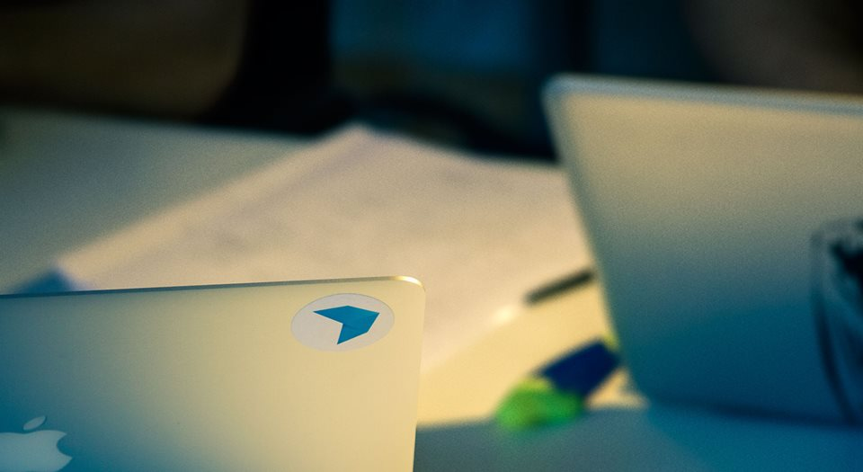 Two laptops on a table, a sticker logo, and papers