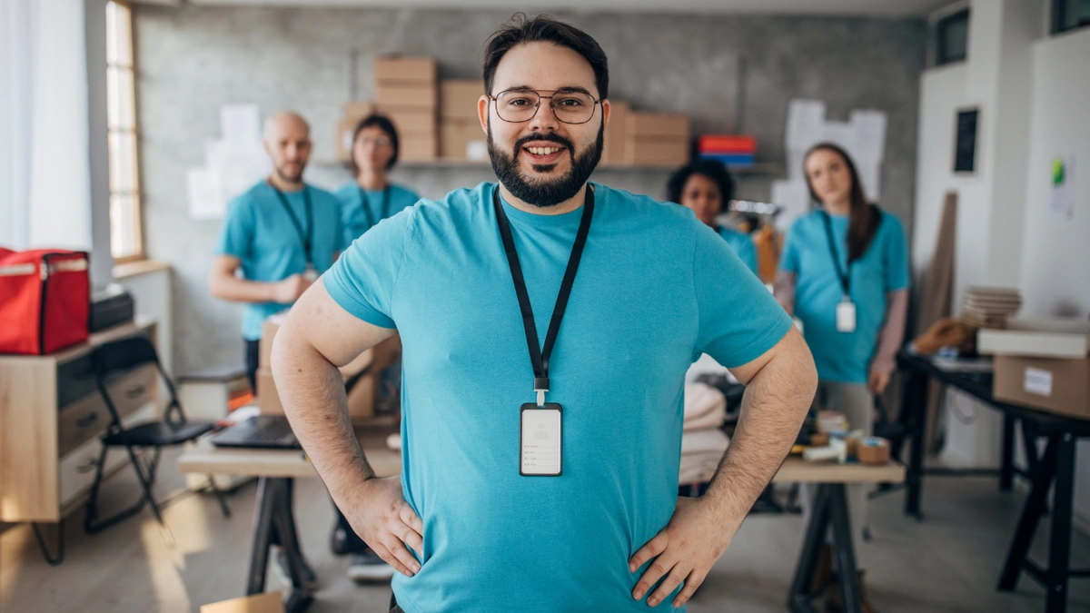 A male volunteer stands in front of four other volunteers with his hands on his hips, smiling.