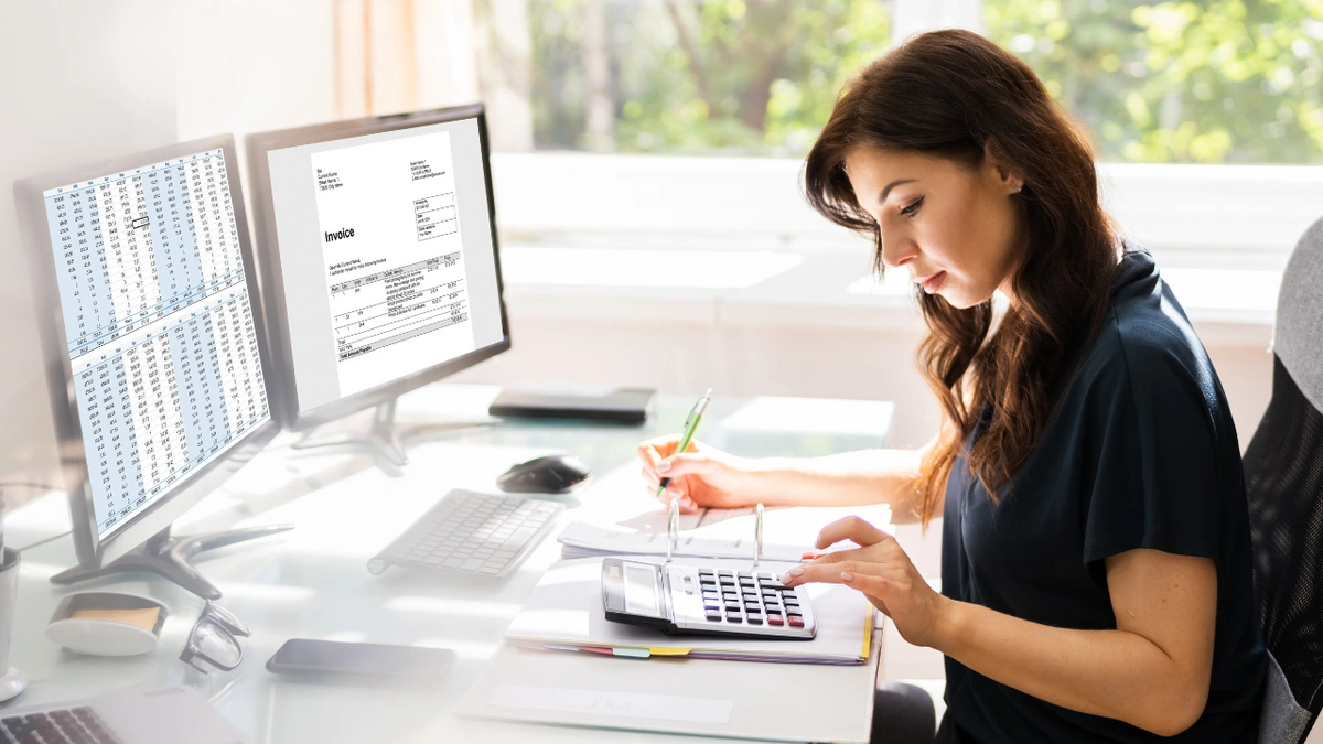 A female accountant looking at a spreadsheet and invoice and using a calculator