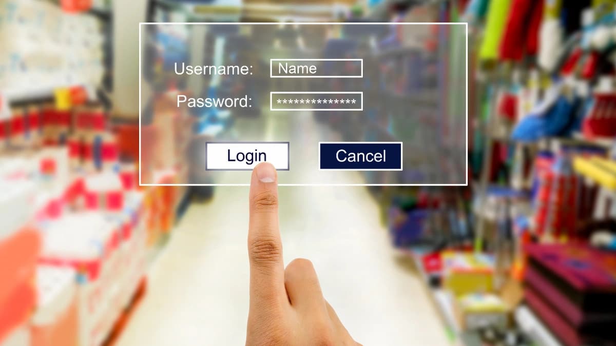 A person's finger in the foreground clicking a "login" button that is part of a login screen including username and password with a blurred background that looks like a hardware store.