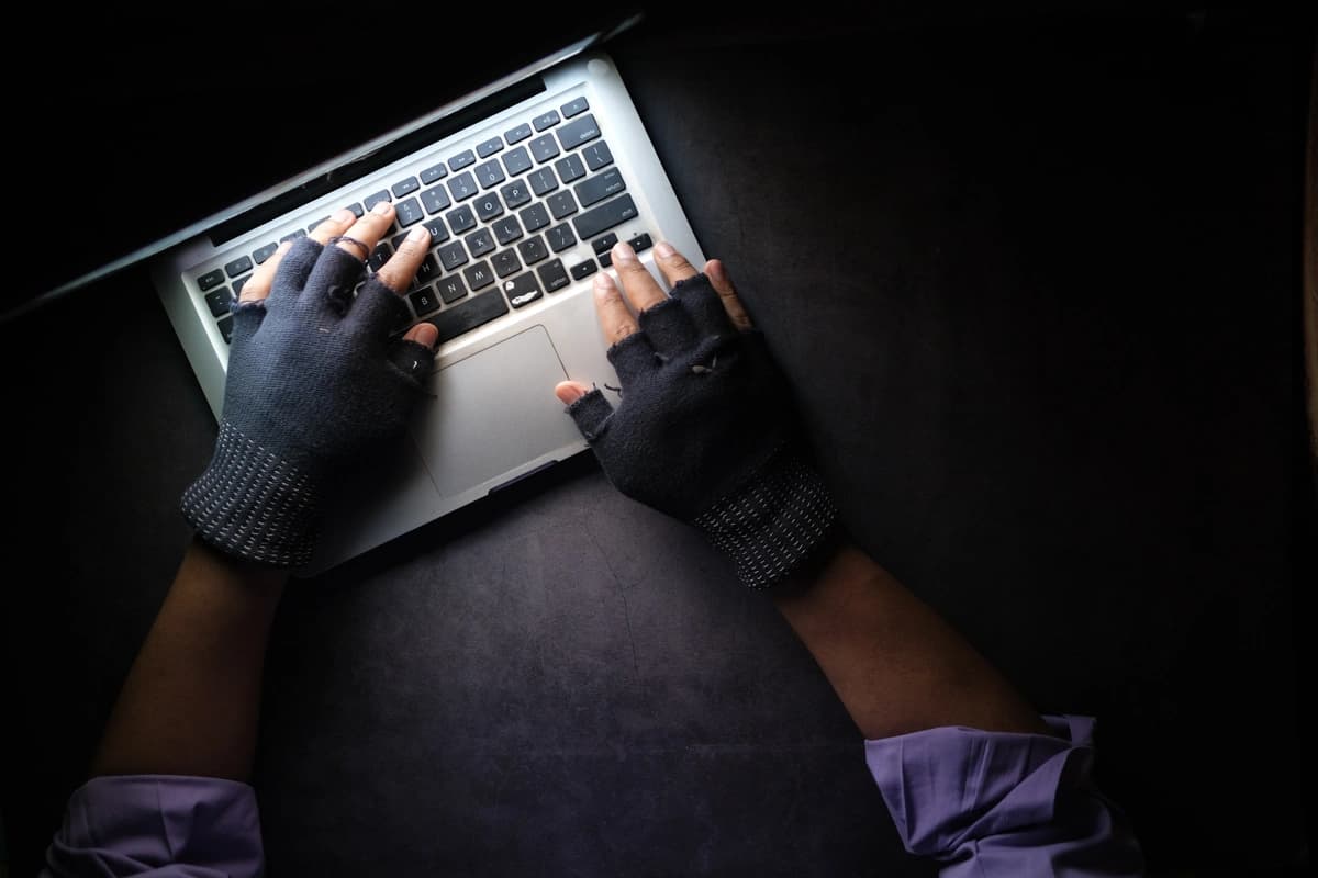 A person in a purple shirt typing on a computer in the dark while wearing fingerless gloves.